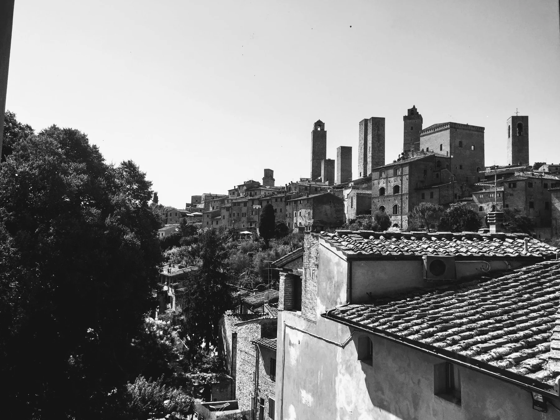 Black-and-white hill town of medieval stone towers rising above tiled rooftops and trees.