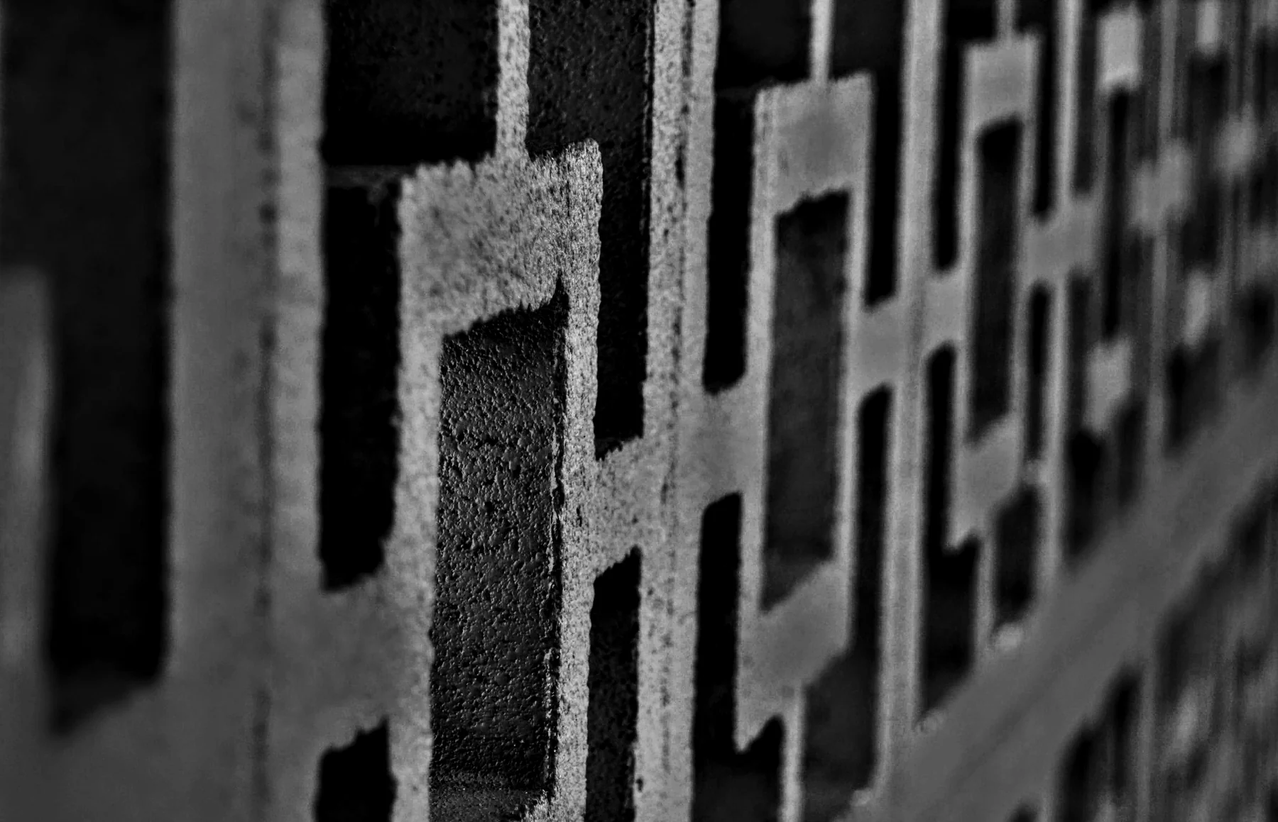 Close, angled black-and-white view of a patterned breeze-block wall receding into blur.