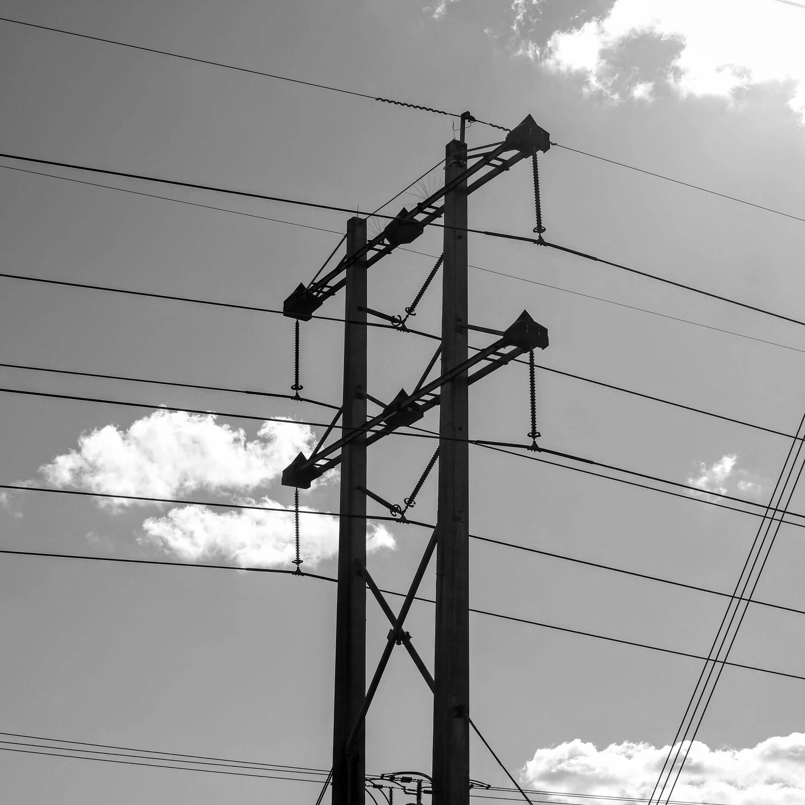 Black-and-white utility poles and crossing power lines against a sky of scattered clouds.