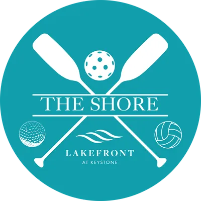 Teal circular logo for The Shore Lakefront at Keystone with crossed paddles and sport balls.