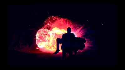 Silhouette carrying another person away from a fiery red and orange explosion at night.